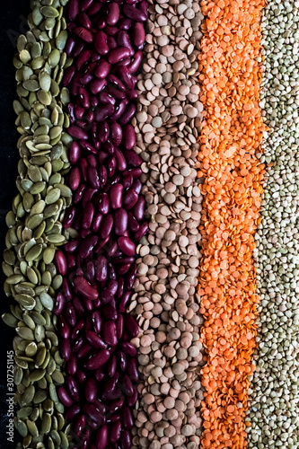 High angle close up of row of dried legumes and seeds in various colours.