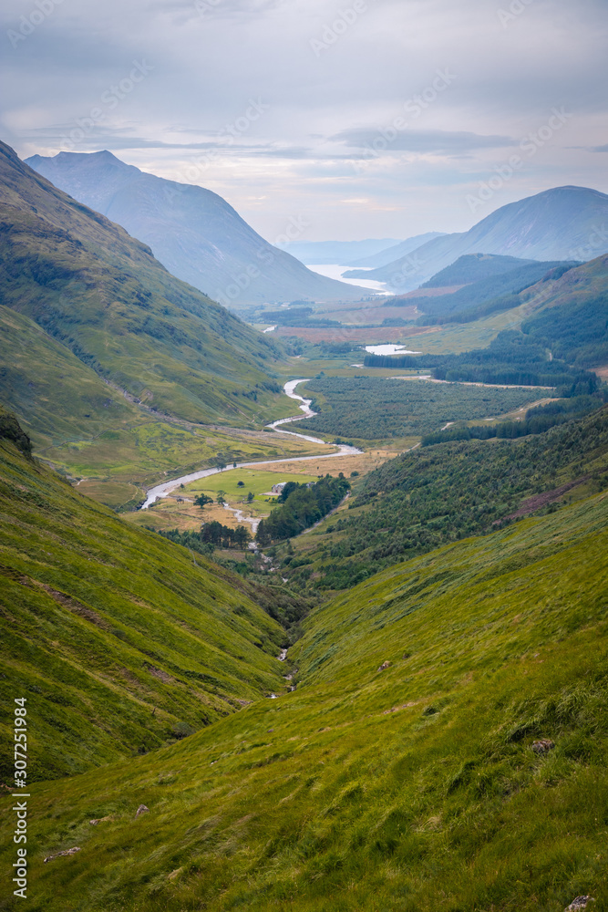 Panoramatic view on Scotland highland valley, during sunset with clouds, green yellow grass painting typical summer view with river in the middle Panoramatic view on Scotland highland valley, during sunset with clouds, green yellow grass painting typical summer view with river in the middle