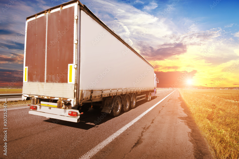 A big truck and trailer on the countryside road against a sky with a sunset A big truck and trailer on the countryside road against a sky with a sunset