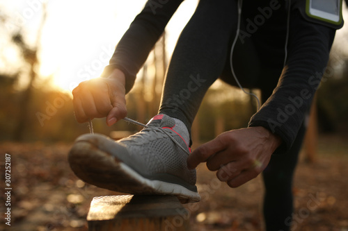 Close-up of black sportswoman tying shoelace in nature at sunset.
