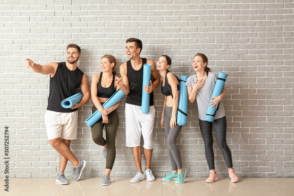 Group of people with yoga mats near brick wall