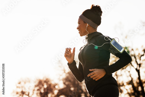 Fototapeta Naklejka Na Ścianę i Meble -  Happy black sportswoman jogging while exercising in nature.