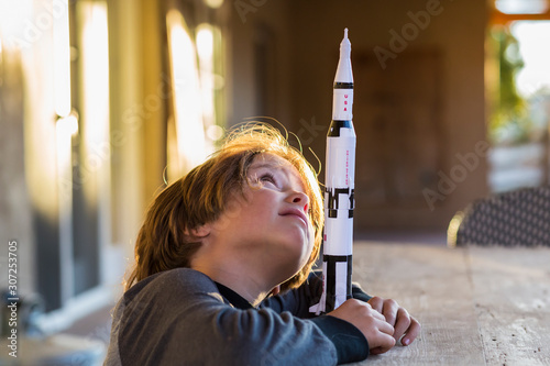 A boy playing with a toy Nasa Saturn 5 rocket, day dreaming about space flight.