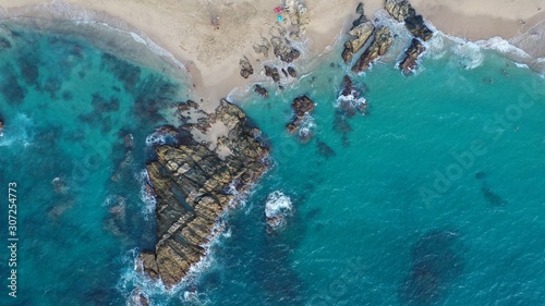 Aerial view of crashing waves on rocks and beach. Drone view of sea waves and beautiful rocky coast. Background texture of a sandy shore and blue turquoise water.