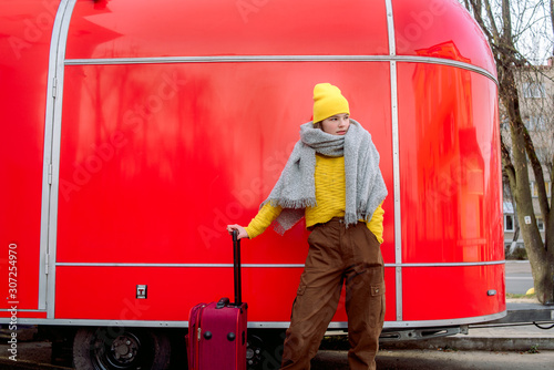 girl runs with a red suitcase on a red background. Large retro vintage van. Old car. Traveling in the winter. Girl in a yellow bright hat and knitted sweater. Travel concept.copy space