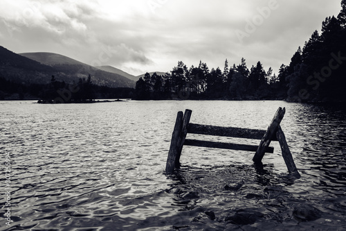 Black and white dramatic view on scottish lake with old woden installation