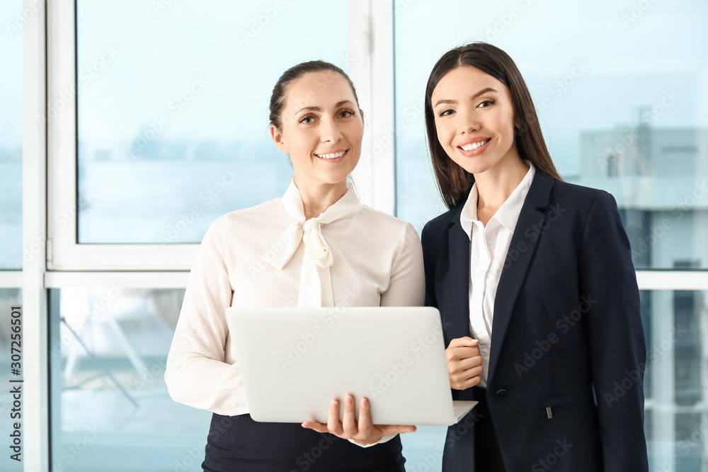 Beautiful businesswomen with laptop discussing issue in office Beautiful businesswomen with laptop discussing issue in office