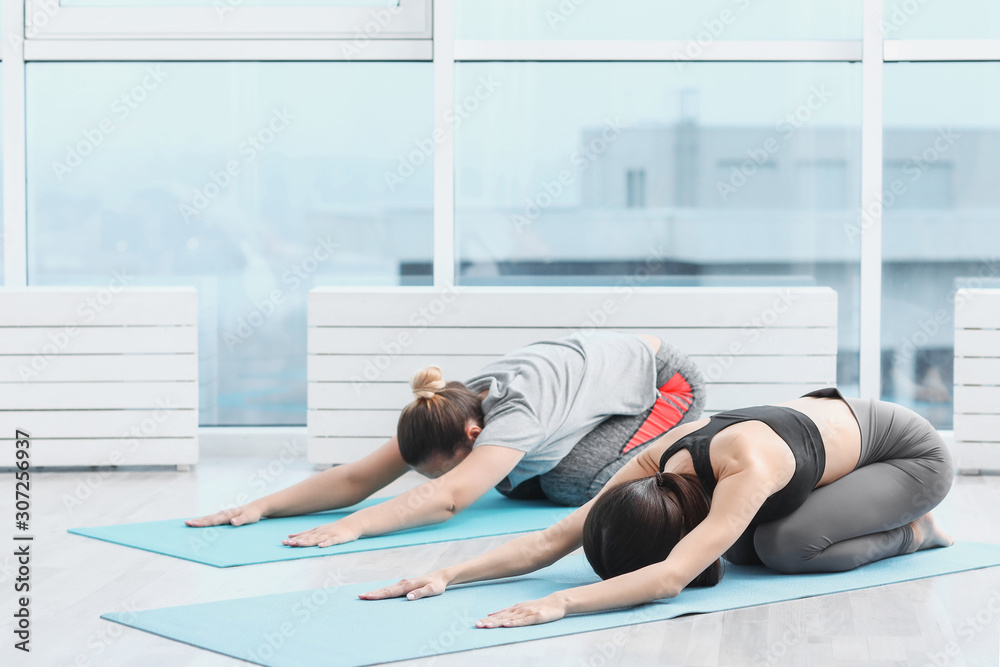 Naklejka premium Sporty young women practicing yoga in gym