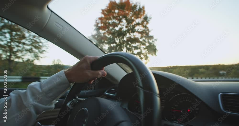 Closeup view of adult male driver hands on steering wheel driving car across the summer twilight. Man drives nano vehicle. Slow-motion. Auto transport. Navigating. Business man traveling alone.