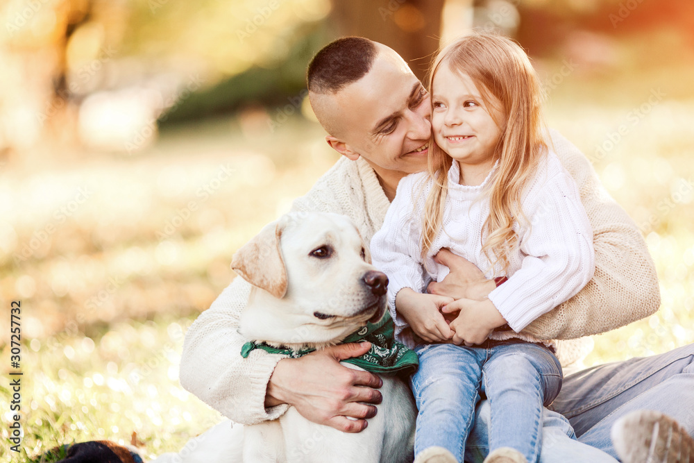 Happy father and daughter with dog labrador is having fun are sitting on green grass in park. Happy father and daughter with dog labrador is having fun are sitting on green grass in park.