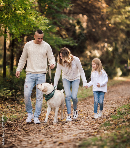 Happy beautiful family with dog labrador is having fun together walking the in park. © zadorozhna