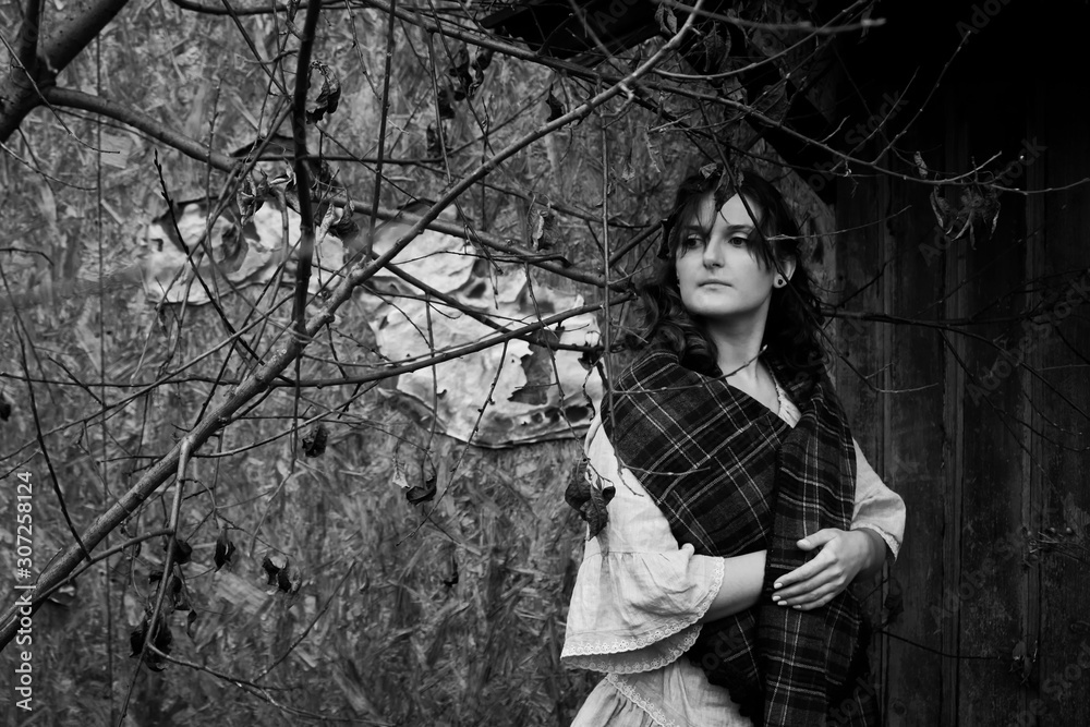 Black and white portrait of a woman against the wall of an old abandoned house. The girl's face in monochrome against the background of overgrown bushes and trees of the building Black and white portrait of a woman against the wall of an old abandoned house. The girl's face in monochrome against the background of overgrown bushes and trees of the building