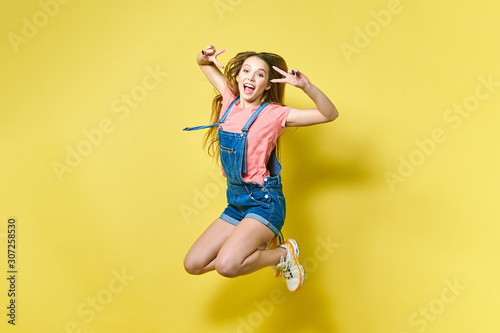 Girlish, funky, happiness, dream, fun, joy, summer concept. Very excited happy cute girl is jumping up, in summer outfit, on yellow background