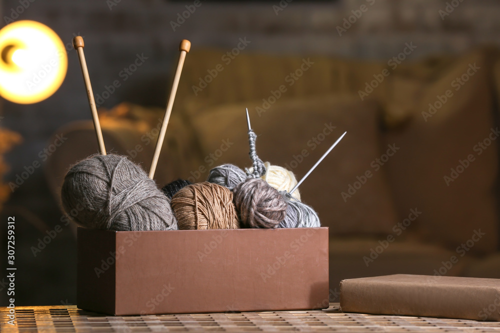 Naklejka premium Box with knitting yarn and needles on table in room