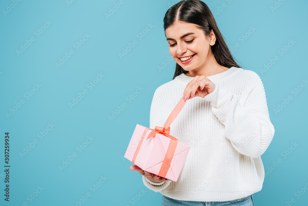 smiling pretty girl in white sweater unwrapping gift box isolated on blue smiling pretty girl in white sweater unwrapping gift box isolated on blue