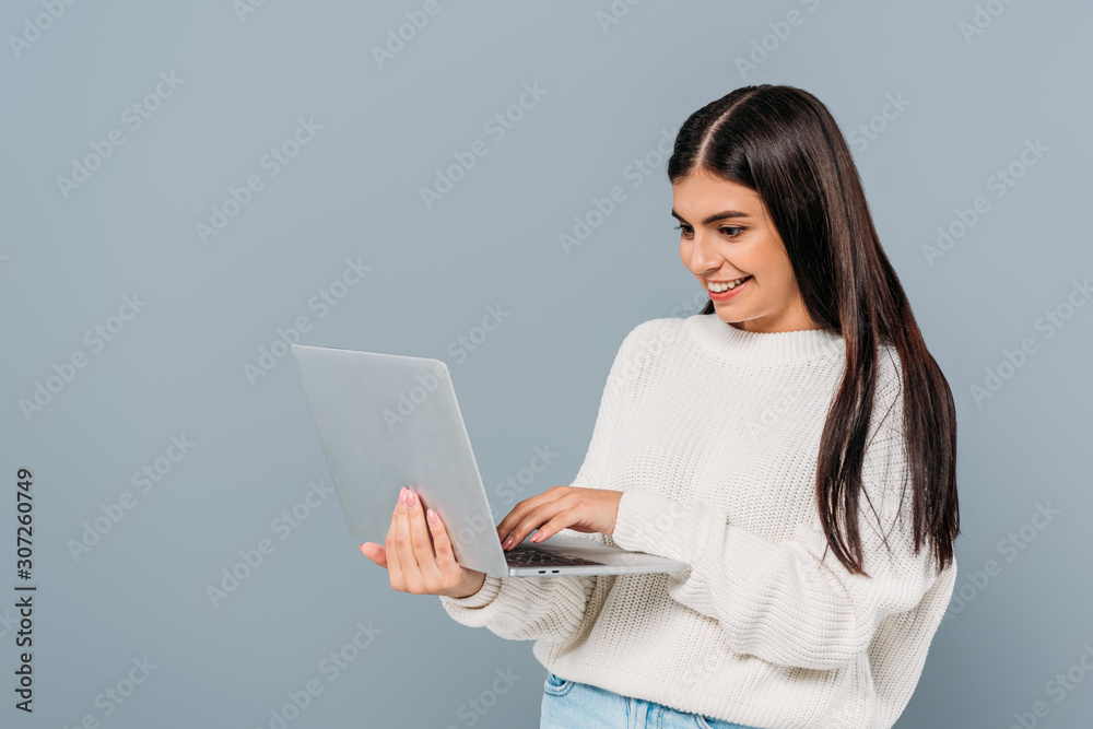 smiling pretty brunette girl in white sweater using laptop isolated on grey smiling pretty brunette girl in white sweater using laptop isolated on grey