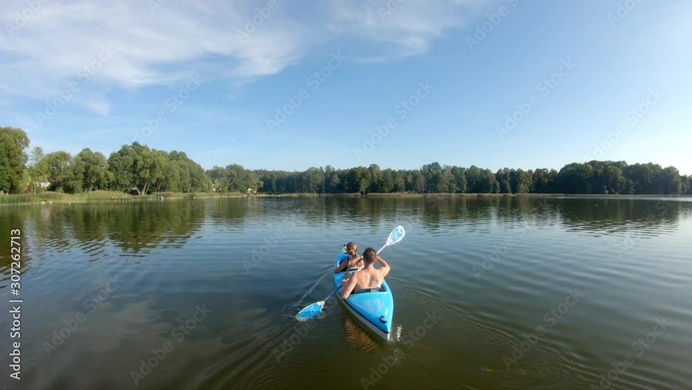 Drone following two kayakers paddling on a lake in a blue kayak during a sunny day in summer. Drone following two kayakers paddling on a lake in a blue kayak during a sunny day in summer.