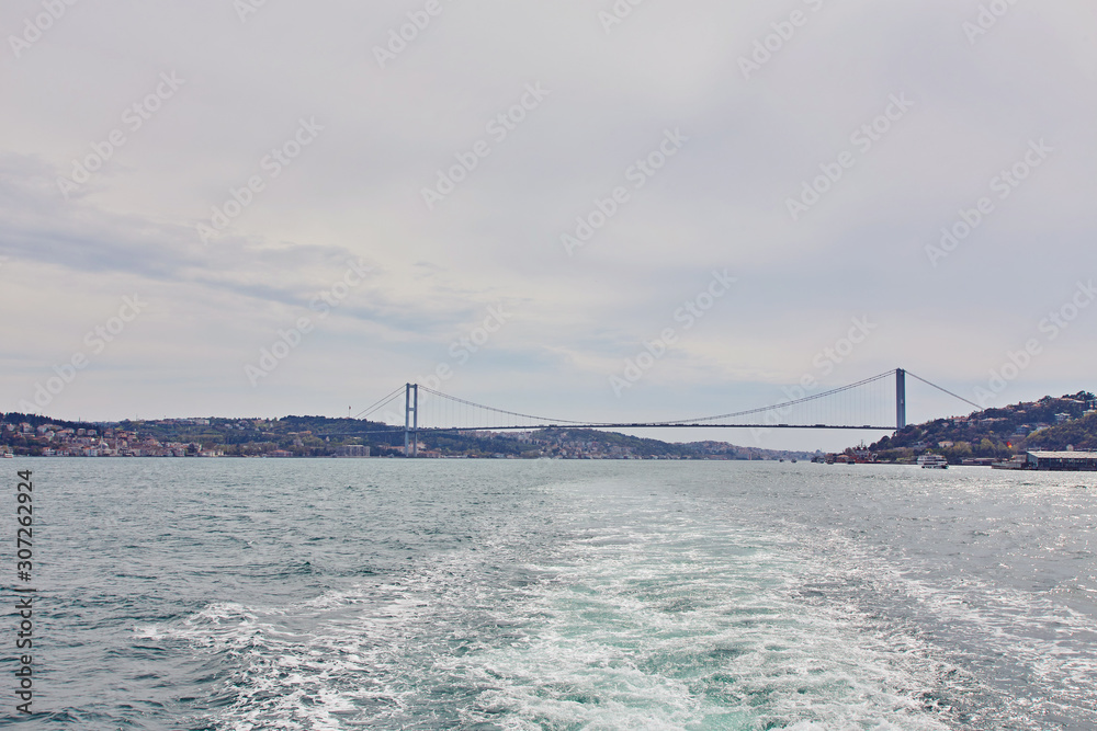 Ships passing through Bosphorus Bridge with background of Bosphorus strait on a sunny day with background cloudy blue sky and blue sea in Istanbul, Turkey.