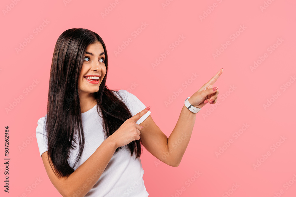 smiling pretty brunette girl pointing with fingers at copy space isolated on pink smiling pretty brunette girl pointing with fingers at copy space isolated on pink
