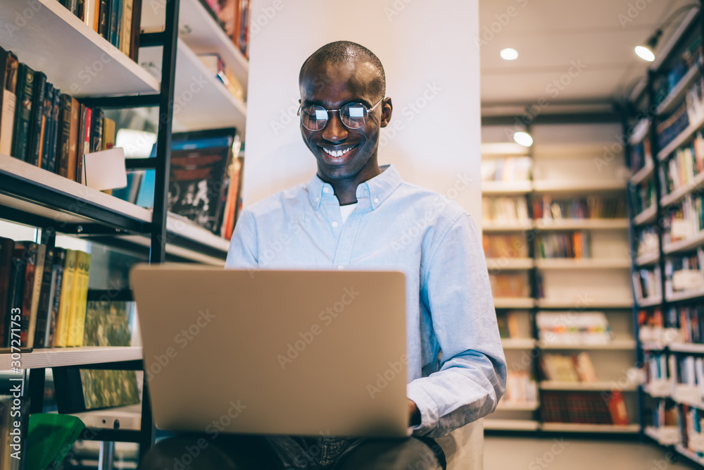 Smiling black student with laptop in library Smiling black student with laptop in library