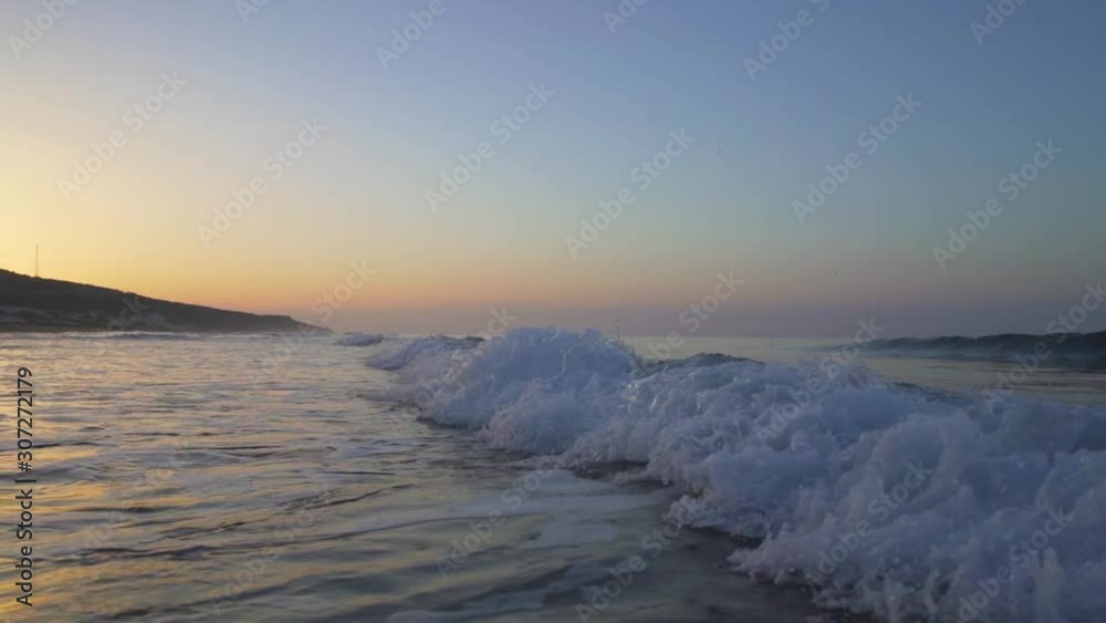 Slow motion of waves on empty remote sand beach during sunrise in summer