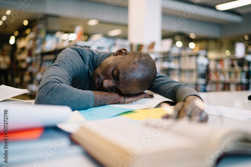 African American man with book sleeping in library