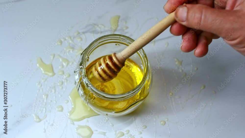 hand picks honey with a wooden spoon from a glass jar hand picks honey with a wooden spoon from a glass jar