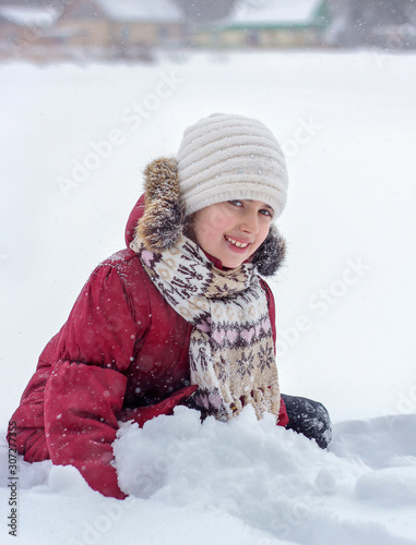 A little girl sits in the snow and plays with the snow.