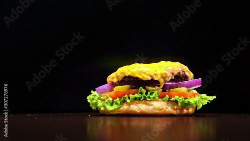Craft burger is cooking on black background in black food gloves. Consist: sauce, lettuce, tomato, red onion, pickle, cheese, bacon, air bun and marbled meat beef. Not made ideal. Looks real, loving photo