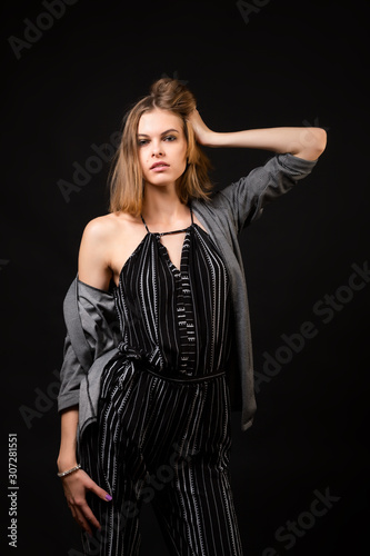 Young beautiful woman wearing in black overalls and cardigan  posing over black background, top view. Studio shot of  brunette woman against isolated background