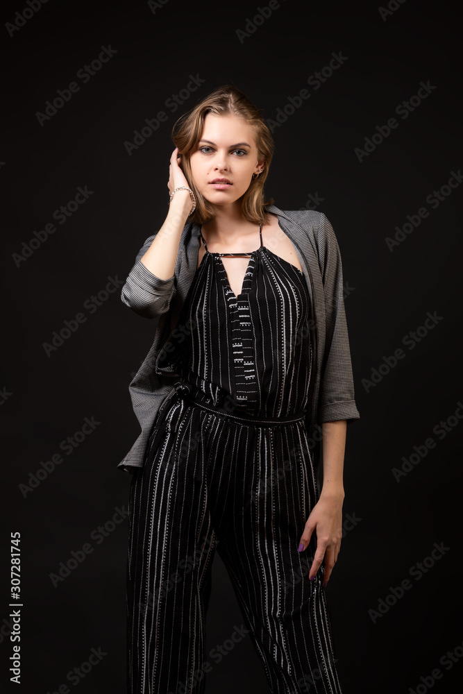 Woman model teaches to pose. High Fashion model girl  posing in studio, portrait of beautiful womanin black overalls and cardigan on  black isolated background