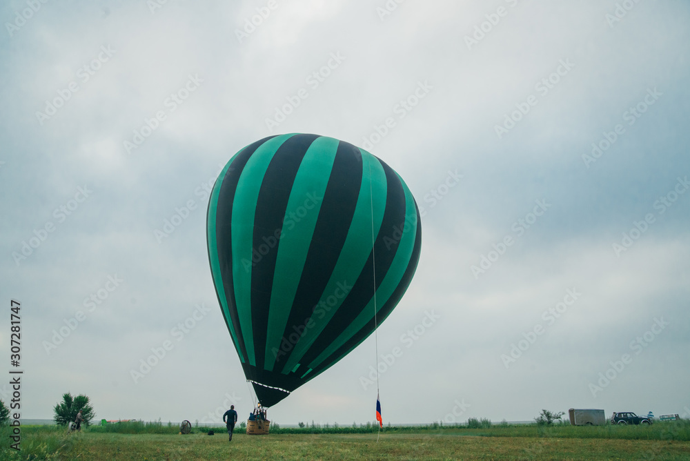 Obraz premium Inflating, unpack and flying up hot air balloon watermelon. Burner directing flame into envelope. Take off aircraft fly in morning blue sky. Start hot air burning to inflate gas fire to air balloon.