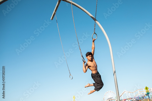 A young man athlete working out on traveling rings on muscle beach, Santa Monica, California