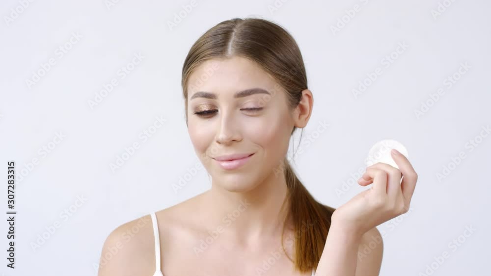 Medium shot of beautiful young woman with dramatic makeup look standing isolated on grey background and gently swiping cotton pad over her left eye. Woman removing eye makeup Medium shot of beautiful young woman with dramatic makeup look standing isolated on grey background and gently swiping cotton pad over her left eye. Woman removing eye makeup