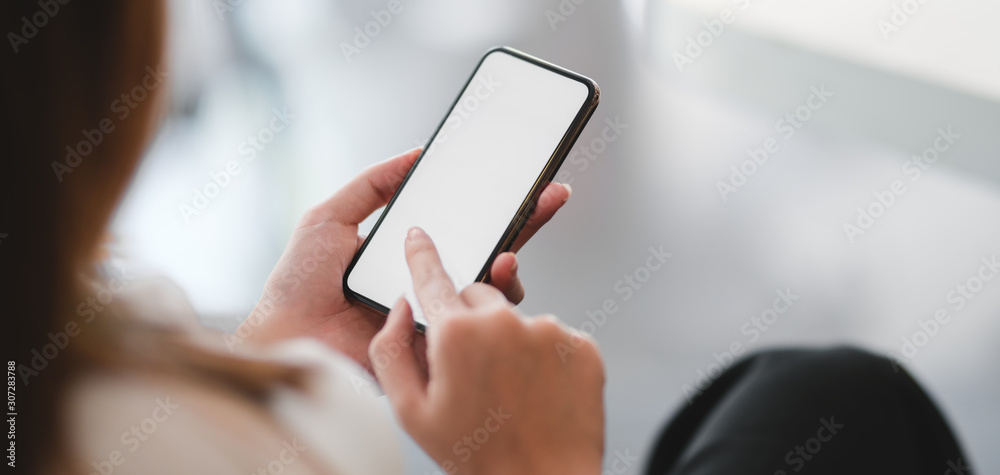 Cropped shot of businesswoman using smartphone in blurred office room