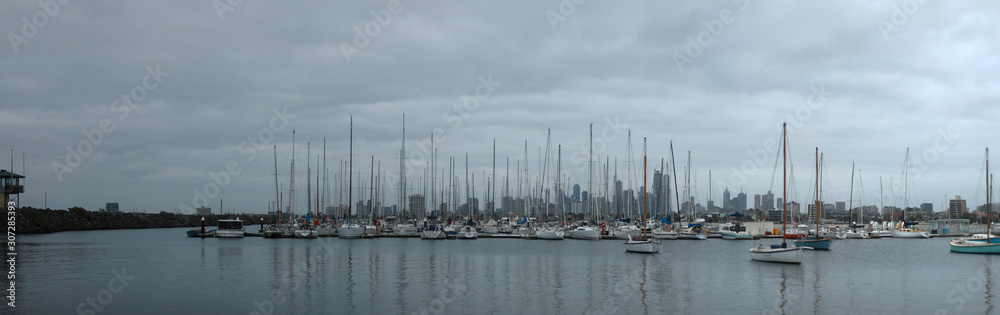 panoramic view of leisure boats tyed up in a rocky bay at St Kilda pier with the Melbourne city skyline stretching across the background in the late afternoon, Australia
