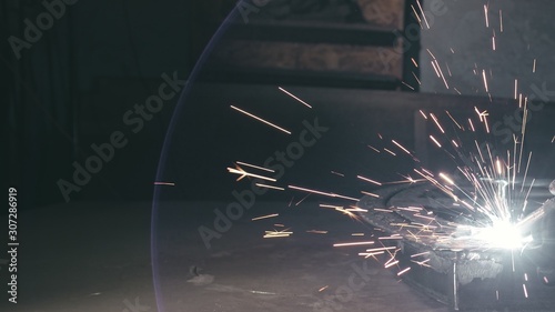 Forge workshop. Smithy. Worker in a welding hood helmet welds a part by electric welding. Sparks are reflected in the protective screen. Blacksmith makes iron product for manufacture. Slow motion. photo
