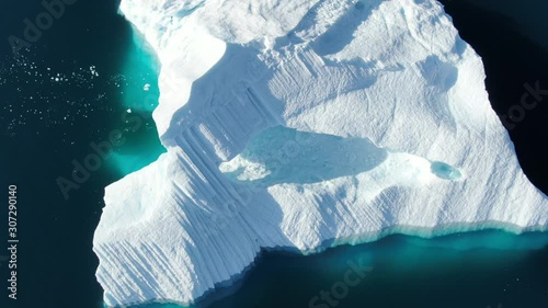 Aerial rotating drone top close-up view of a white iceberg floating in the arctic Baffin sea, showing high details of ice texture, with deep blue and turquoise shades, during a sunny day photo