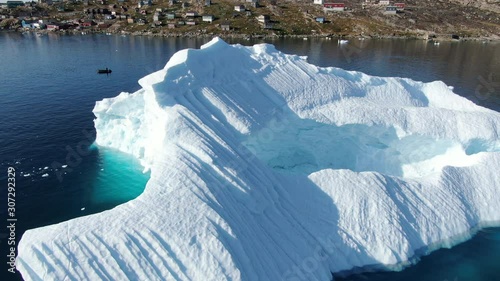 Ascending drone view of the island of Kullorsuaq, Greenland, showing a highly detailed scenery with icebergs floating in the deep blue arctic sea, little houses build on the rocky terrain