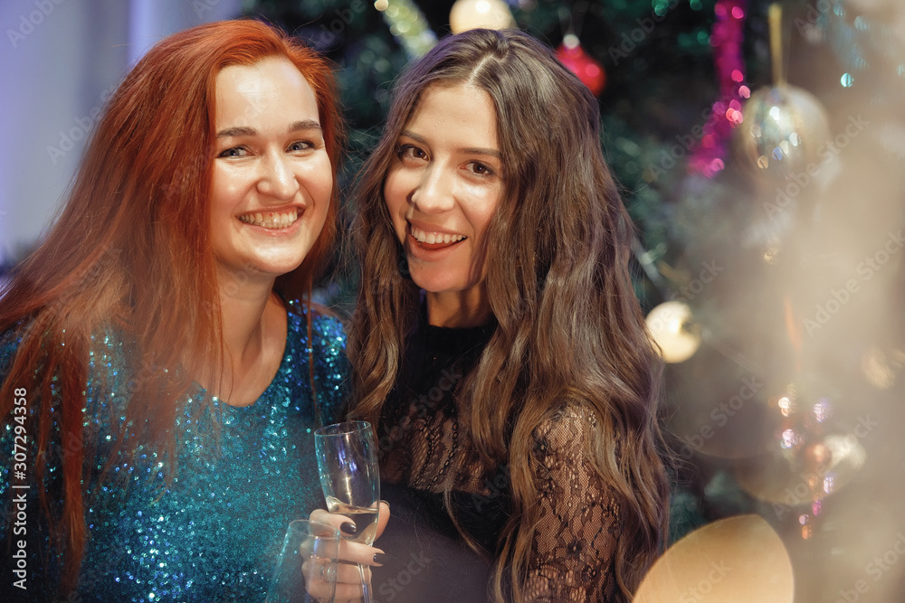 Beautiful women with a glass of champagne near a Christmas tree.