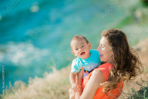 Mother in summer embraces her little son against the background of the rock and the sea shore.