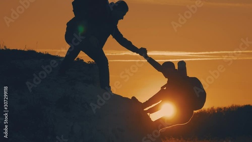 Silhouette of helping hand between two climber. two hikers on top of the mountain, a man helps a woman to climb a sheer stone. couple hiking help each other silhouette in mountains with sunlight.