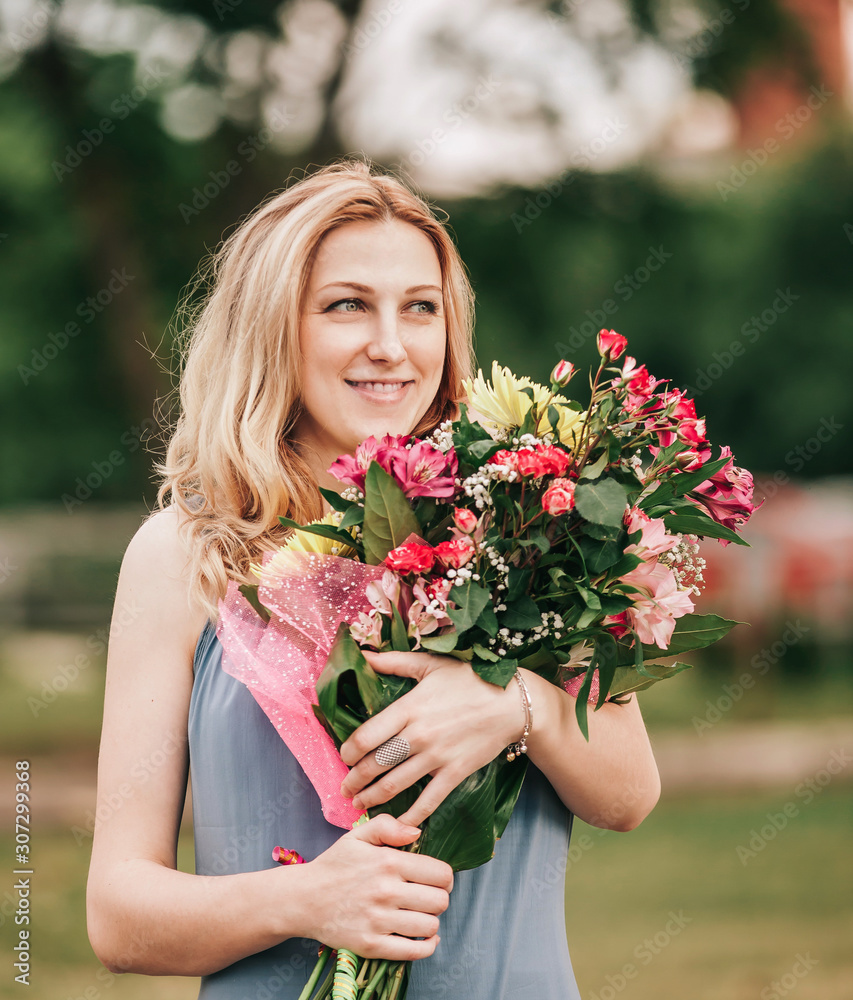 beautiful woman with a bouquet of flowers standing on the grass in the city Park beautiful woman with a bouquet of flowers standing on the grass in the city Park