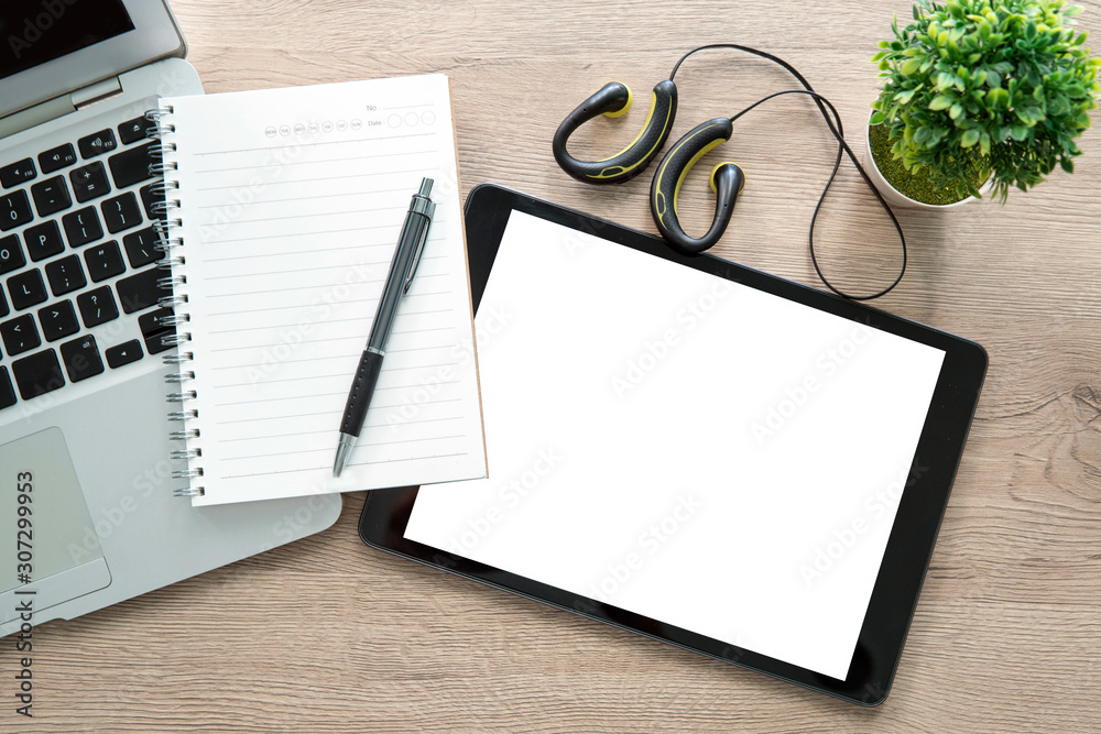 Wood office desk table with blank notebook over tablet computer with pen, earphone. Top view.