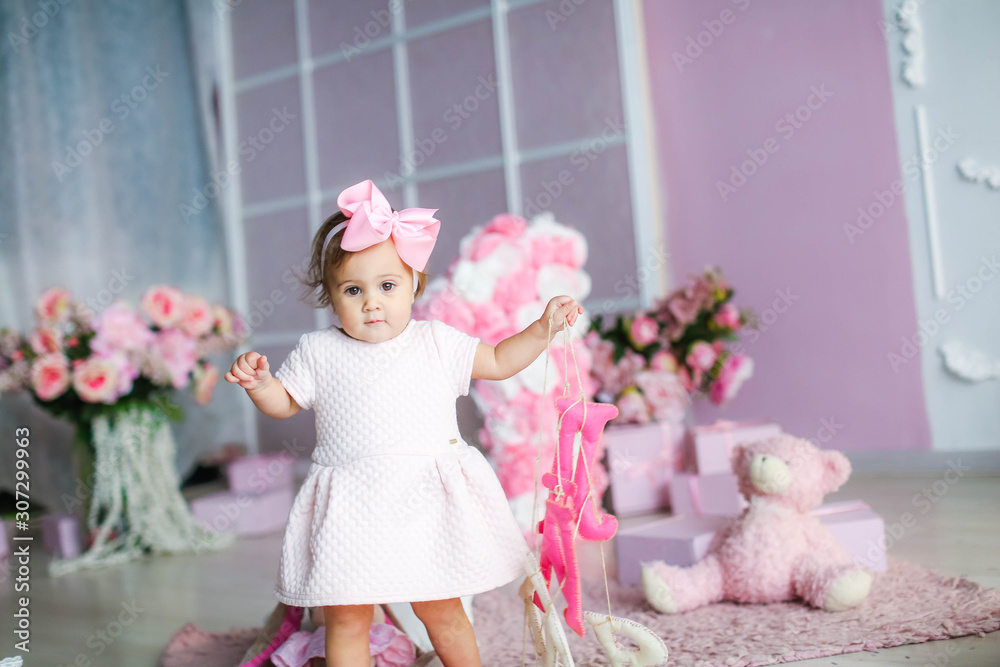 Fototapeta premium Baby with a pink dress on a background of pink adornment with a pink bow on her head.