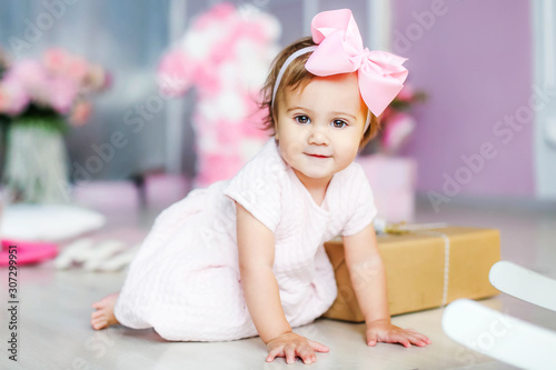 Baby with a pink dress on a background of pink adornment with a pink bow on her head.