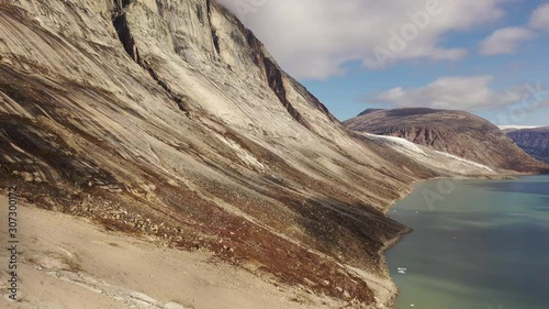 Slow and majestic aerial drone ascending view of the Sam Ford Fjord, Canada, near Greenland, with ice and rock cliffs rising steeply from the shore, with high details of the harsh ground