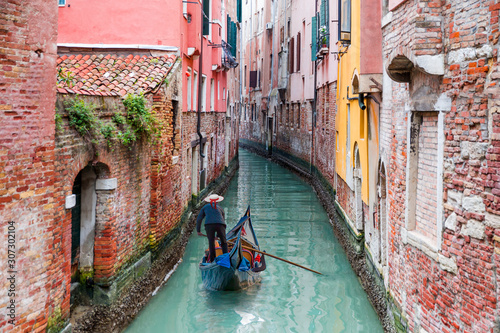 Fotografia Venetian gondolier punting gondola through green canal waters of Venice Italy