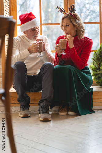 Relaxed mature couple drinking hot cacao near window