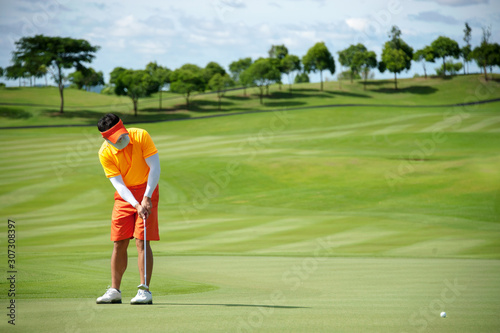 Colorful orange golfer puttng and focus on his golf ball on gree photo